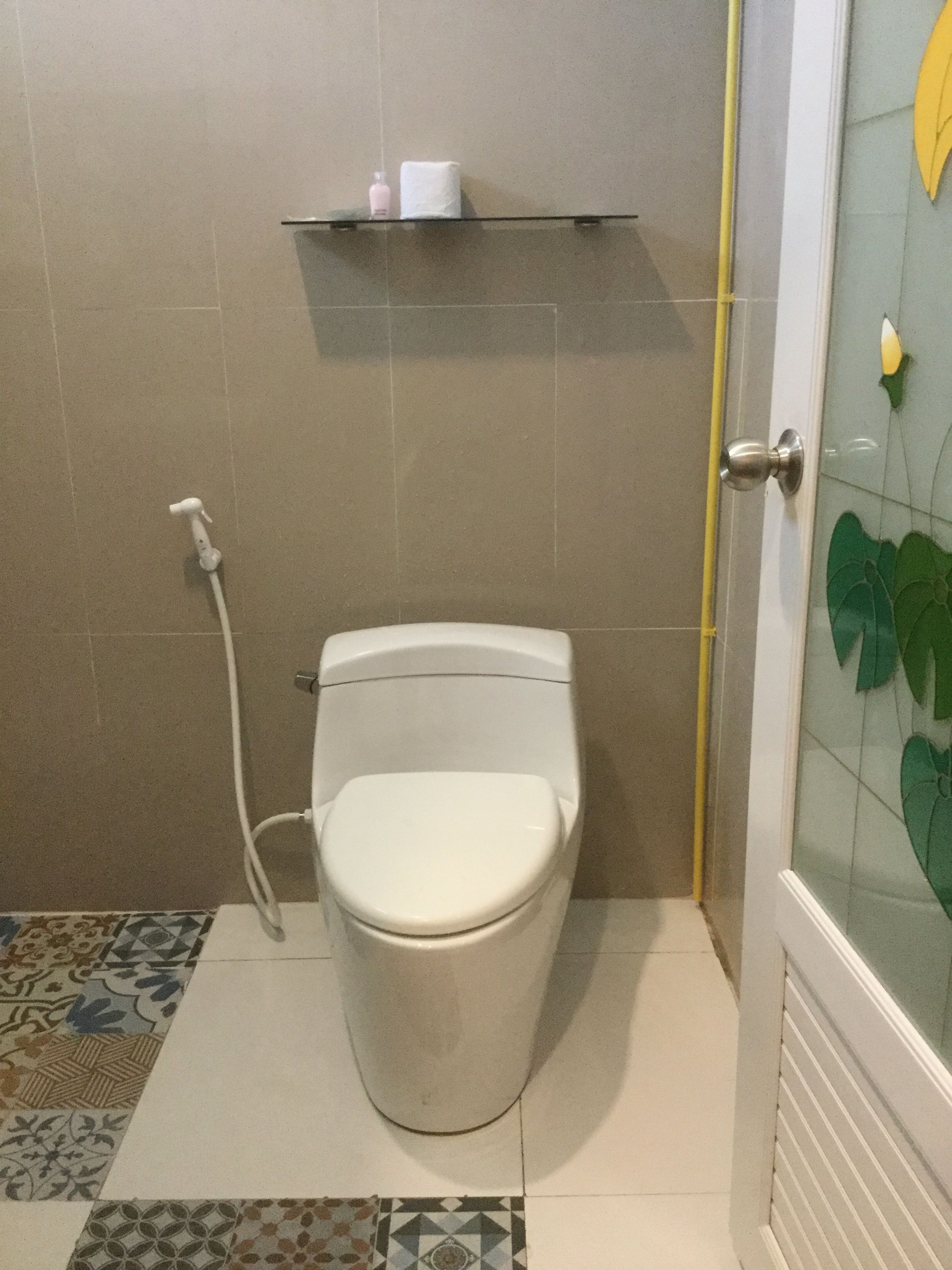 Un baño con inodoro, ducha y puerta de vidrio con diseño floral.
