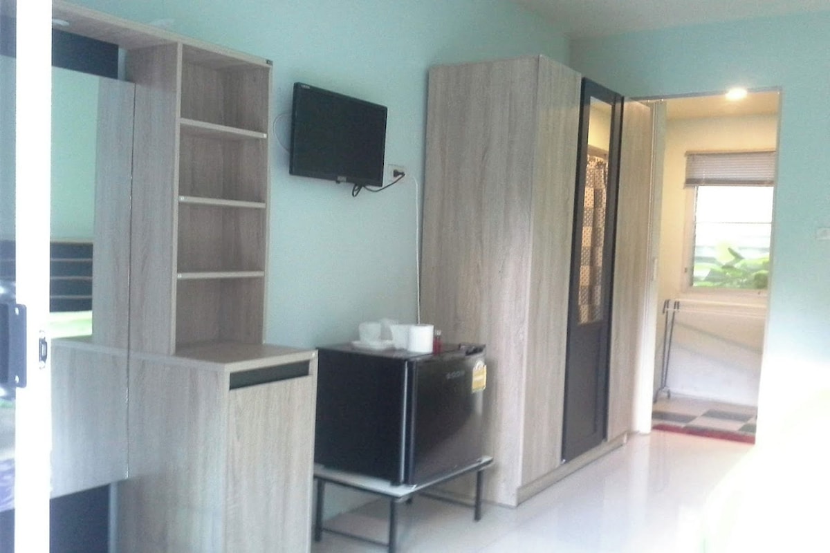 A room with a wardrobe, a small table with a television, and a door leading to another area.
