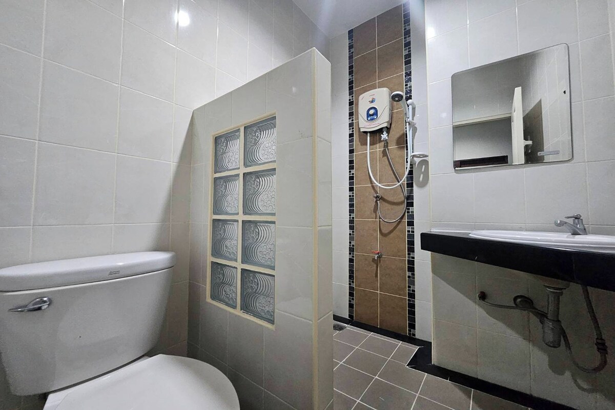 A bathroom with a toilet, a shower with a control panel, and a sink with a mirror.