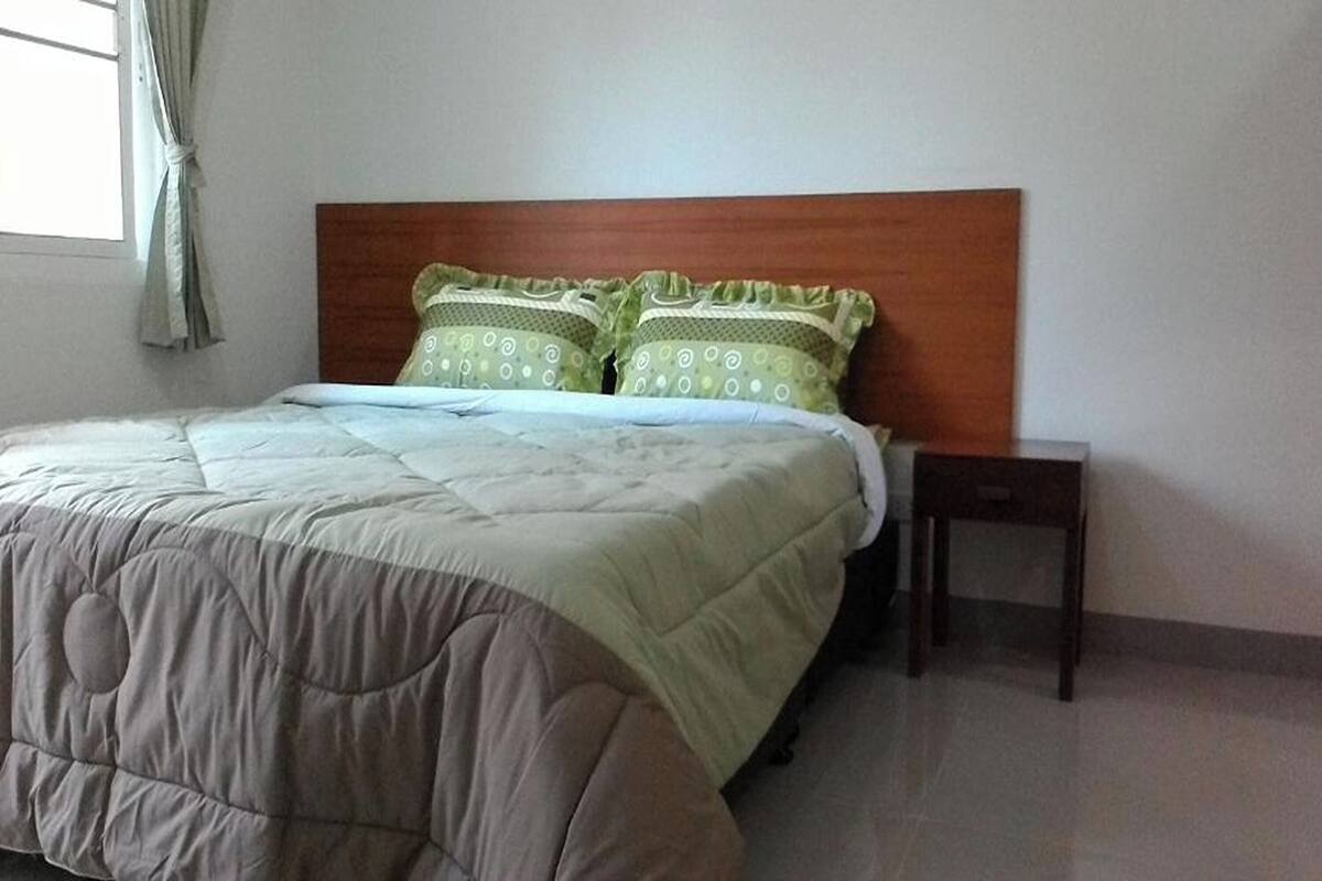 A neatly made bed with a beige and white duvet, two patterned pillows, and a wooden headboard.