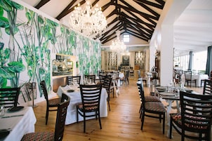 Um restaurante com chão de madeira, toalhas de mesa brancas e cadeiras estampadas.