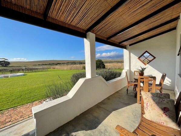 A covered patio with a view of a green field and distant hills.