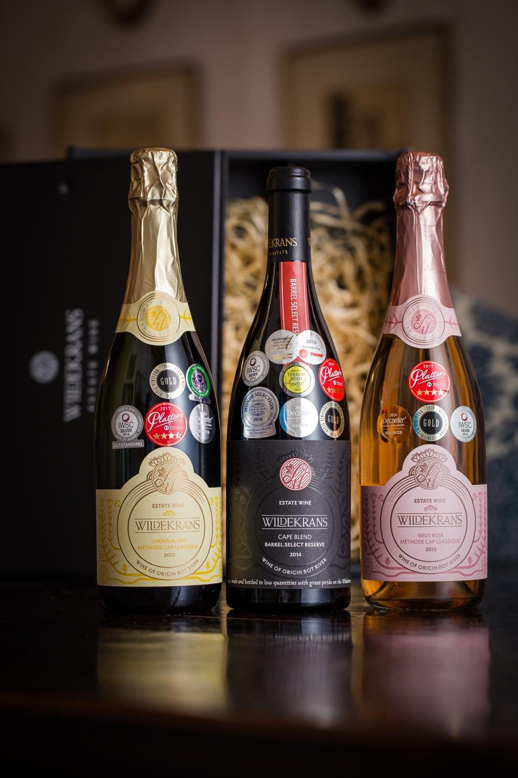 Three bottles of wine with labels and awards, placed on a reflective surface.