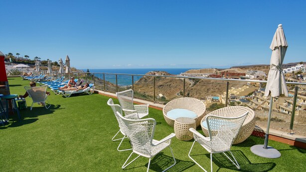 A terrace with white wicker furniture, a pool table, and a view of the ocean and hills. - Balcón del Mar (Puerto Rico)