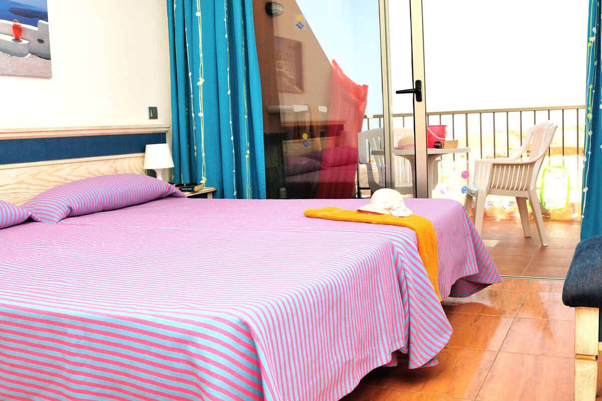 Une chambre d’hôtel avec deux lits, un balcon avec une chaise et une table avec une chaise.