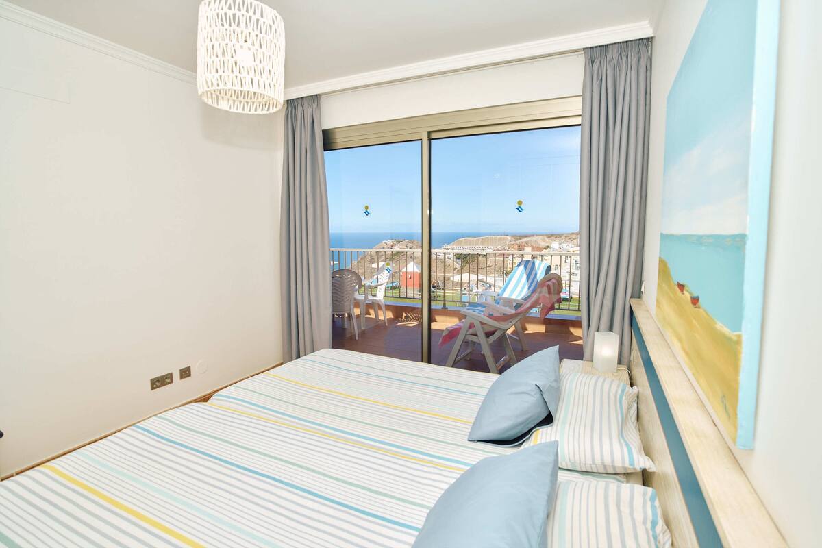 Une chambre d’hôtel avec un grand lit, un balcon donnant sur la ville et un tableau accroché au mur.