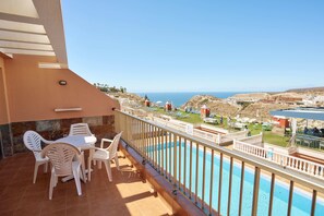 Uma varanda com piscina, cadeiras brancas e vista para o mar e edifícios.
