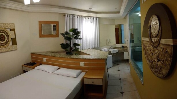 A hotel room with a bed, a wooden vanity with a sink, a large mirror, and a potted plant. - Hotel Luni (São Paulo)