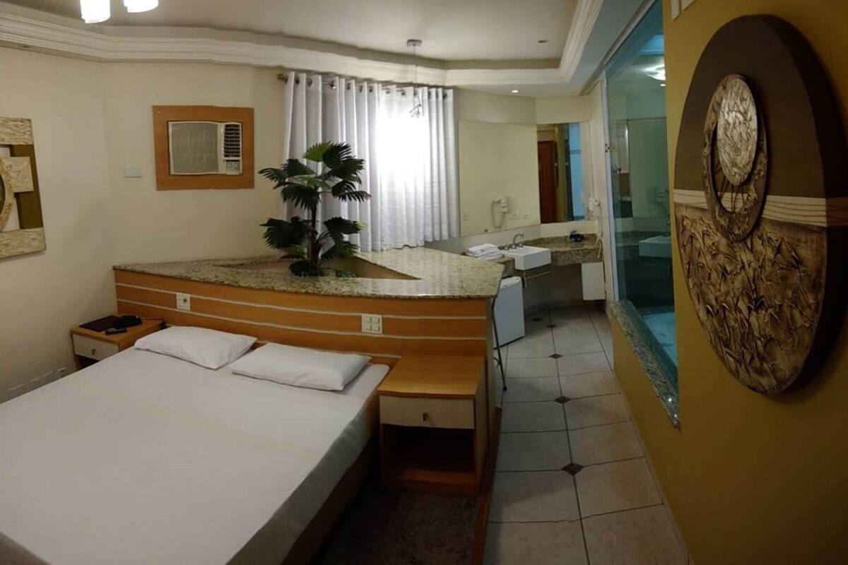 Ein Hotelzimmer mit einem Bett, einem Holznähen mit Waschbecken, einem großen Spiegel und einer Topfpflanze.