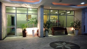 A hotel entrance with glass doors, potted plants, a bench, and a tiled floor. - Hotel Luni (São Paulo)