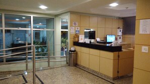 A reception area with a counter, computer monitors, and a trash bin. - Hotel Luni (São Paulo)