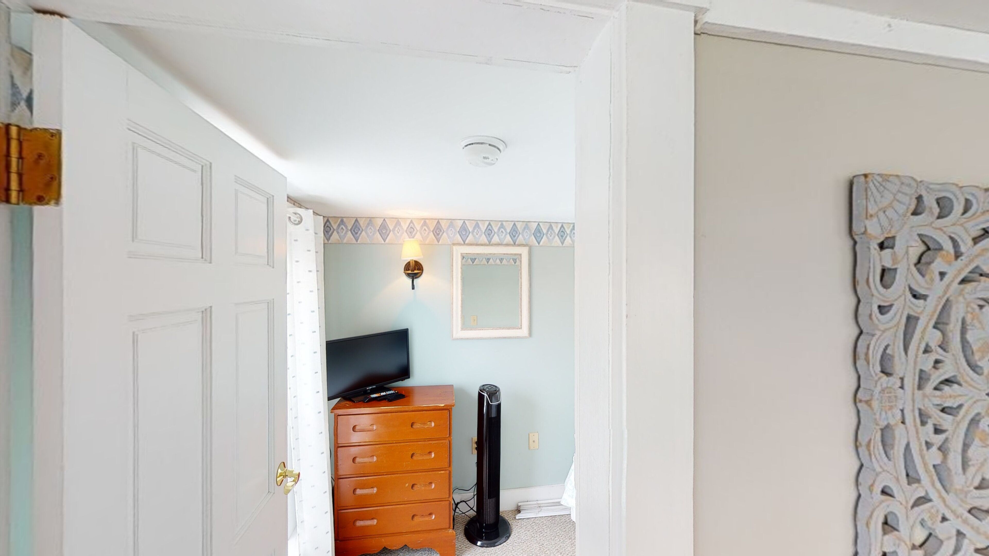 A room with a wooden dresser, a black fan, a television, and a decorative mirror on the wall.