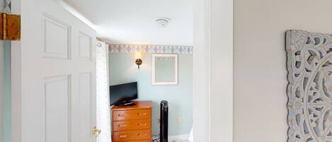 A room with a wooden dresser, a black fan, a television, and a decorative mirror on the wall.