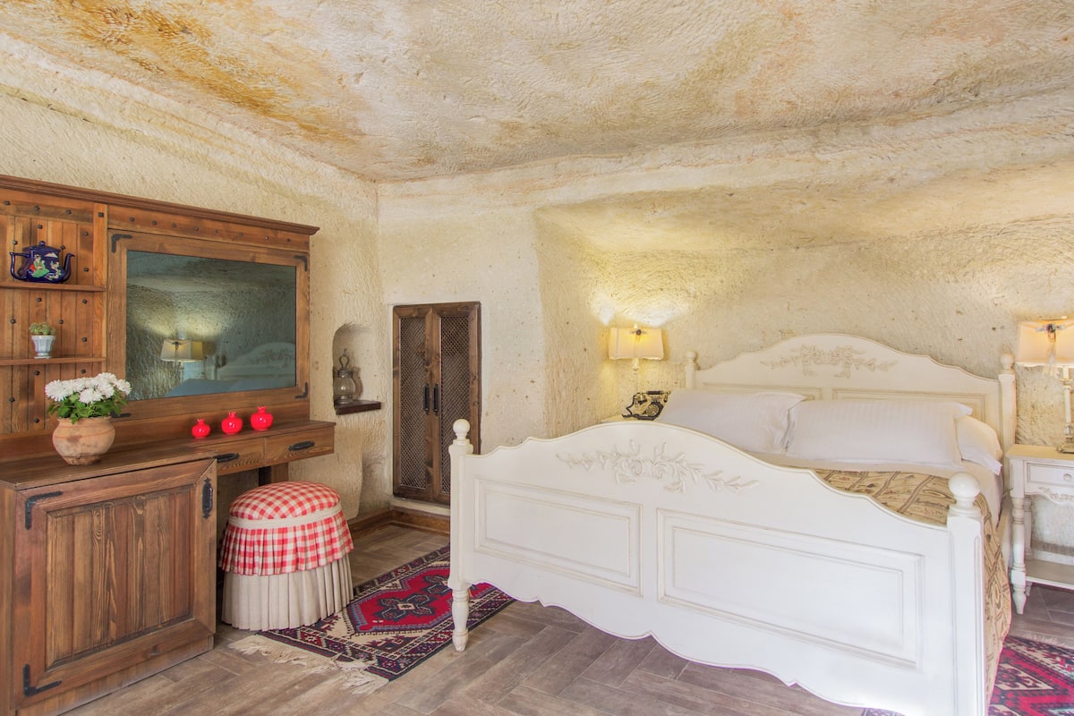 Un dormitorio con un aparador de madera, una cama, un taburete a cuadros rojo y blanco, y una alfombra estampada.