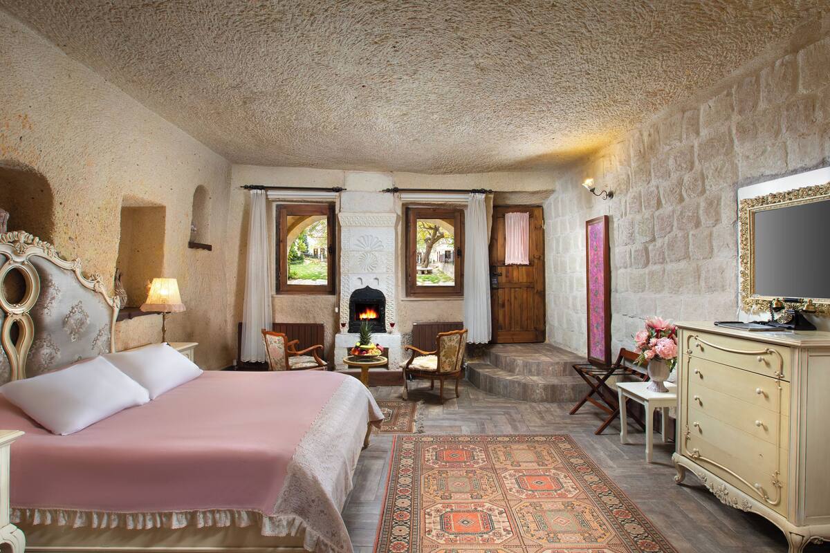 Un dormitorio con cama, chimenea, puerta de madera, cómoda y ventana con cortinas.