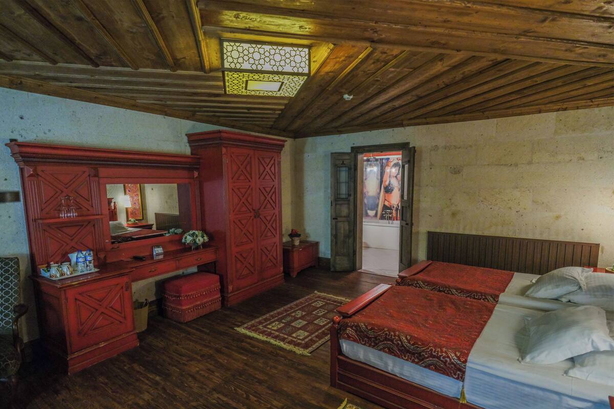 Una habitación tradicional con techo de madera, una cama con colcha roja, un aparador de madera y un espejo.