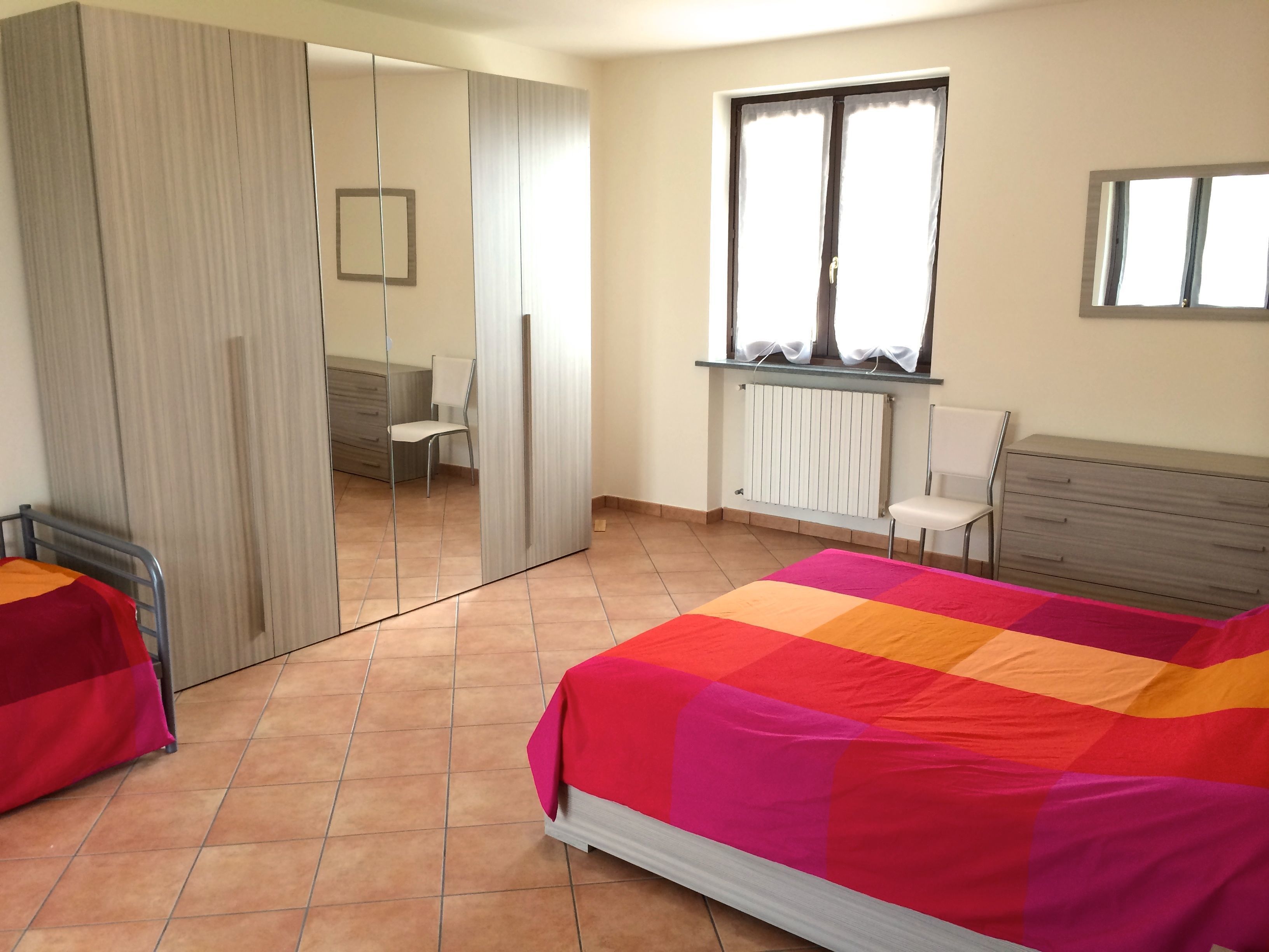 Un dormitorio con cama, una silla, un armario y una ventana.