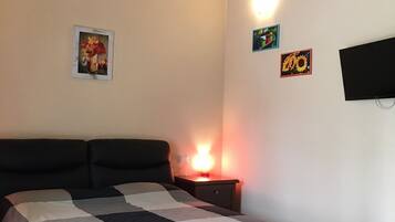 Une chambre à coucher comprenant un lit, une table de chevet, un téléviseur fixé au mur et une lampe fixée au mur.