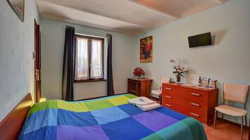 Ein Schlafzimmer mit Bett, Schreibtisch, Stuhl, Kommode, einem Fenster mit Vorhängen und einem Bild an der Wand.