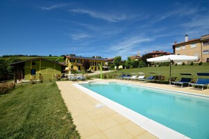 Una piscina con tumbonas, una zona verde y edificios al fondo.