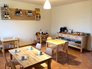 A dining area with wooden tables and chairs, a kitchen with various appliances, and wine bottles displayed on shelves. - The Green GuestHouse (Barolo)