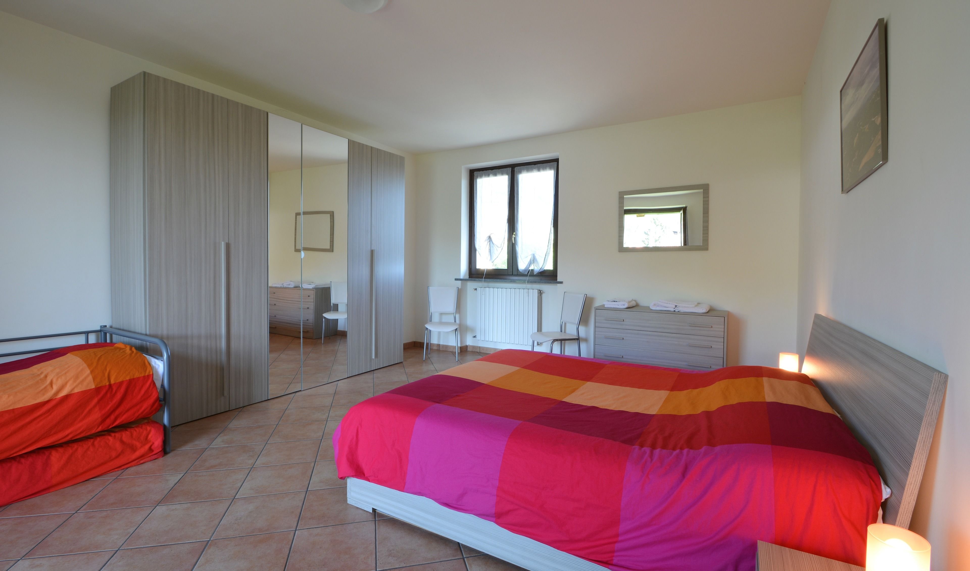 Une chambre à coucher avec un grand lit, une commode, un miroir et une fenêtre.