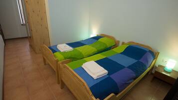 Una stanza con due letti di legno, ognuno con una coperta colorata. Sul lato destro, un comodino con una lampada.