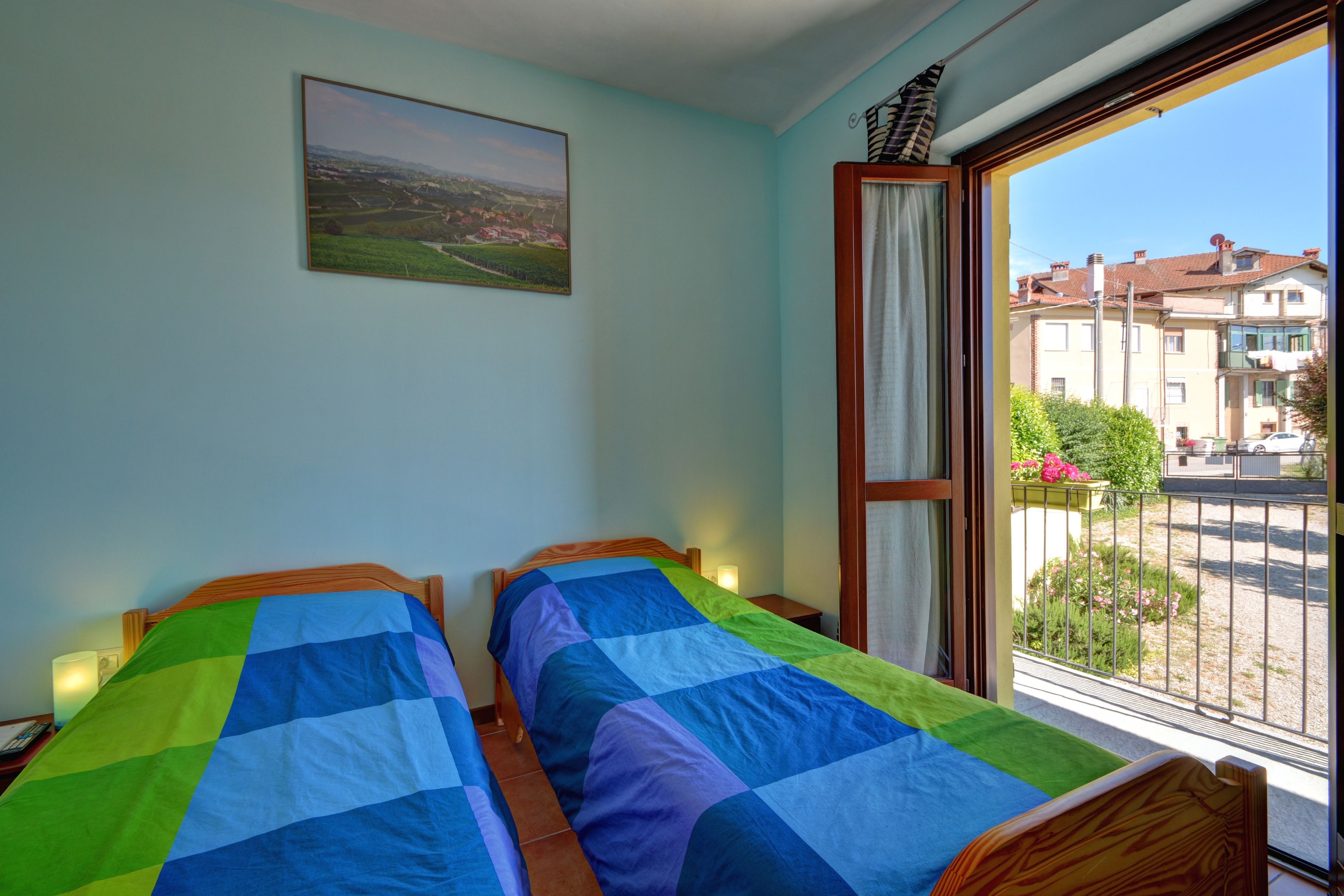 Una habitación con dos camas, una ventana que da a edificios y un cuadro en la pared.