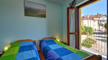 Una habitación con dos camas, una ventana que da a edificios y un cuadro en la pared.