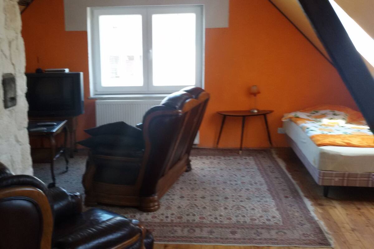 A cozy room with a large window, a television, a sofa, and a bed.