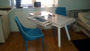 A compact kitchen with a white table, blue chairs, and a window with blinds.
