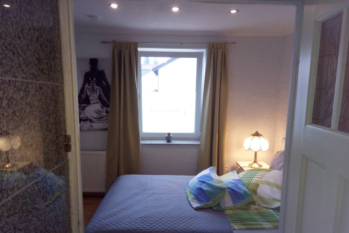 A bedroom with a bed, a window with curtains, a lamp, and a wall with a patterned design.
