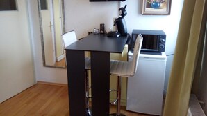 A compact room with a small table, a chair, a television mounted on the wall, a microwave, and a framed picture.