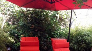 Two red lounge chairs under a red umbrella in a garden setting.