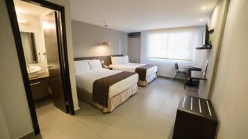 A hotel room with two beds, a desk, a chair, a small table, a mirror, and a window.
