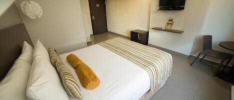 A hotel room with a bed, pillows, a television, a chair, and a small table.