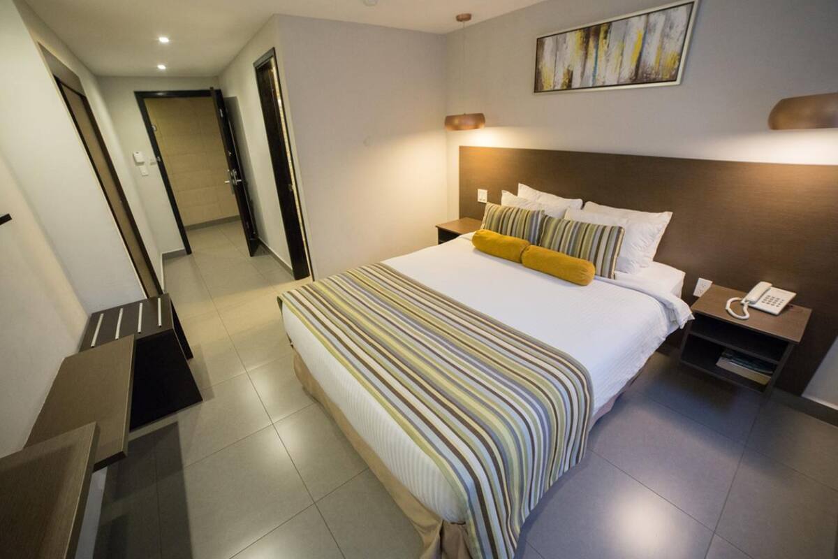 A hotel room with a large bed, a bedside table with a lamp, and a phone.