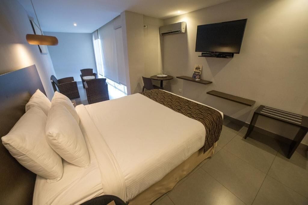 Ein Hotelzimmer mit einem großen Bett, einem an der Wand befestigten Fernseher, einem kleinen Tisch und einem Stuhl.