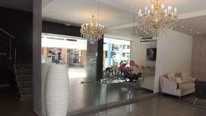 A modern hotel lobby with a chandelier, a sofa, a glass coffee table, and a large vase. - Hotel Ojos del Rio (Panama City)