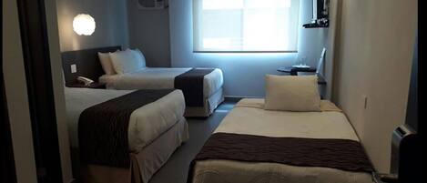 Habitación de hotel con dos camas, una mesita de noche con lámpara, una ventana con persianas y un aire acondicionado instalado en la pared.