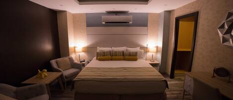 A modern hotel room with a large bed, two bedside tables with lamps, a desk, and a chair.