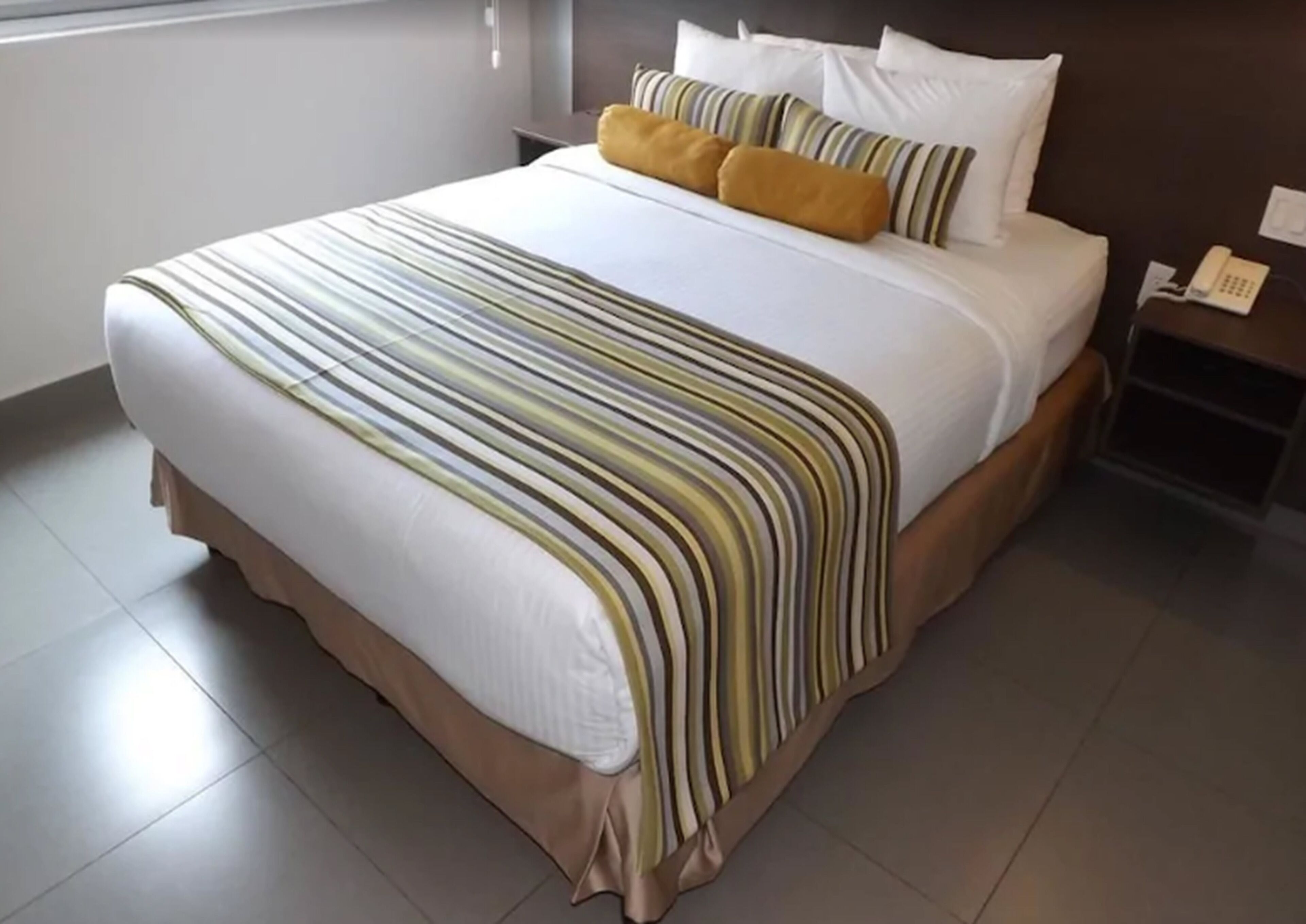 Una habitación de hotel con una cama grande, una mesita de noche con un teléfono y una ventana.