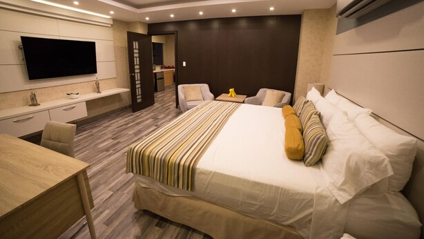 A modern hotel room with a large bed, a desk, a flat-screen TV, and a separate seating area. - Hotel Ojos del Rio (Panama City)