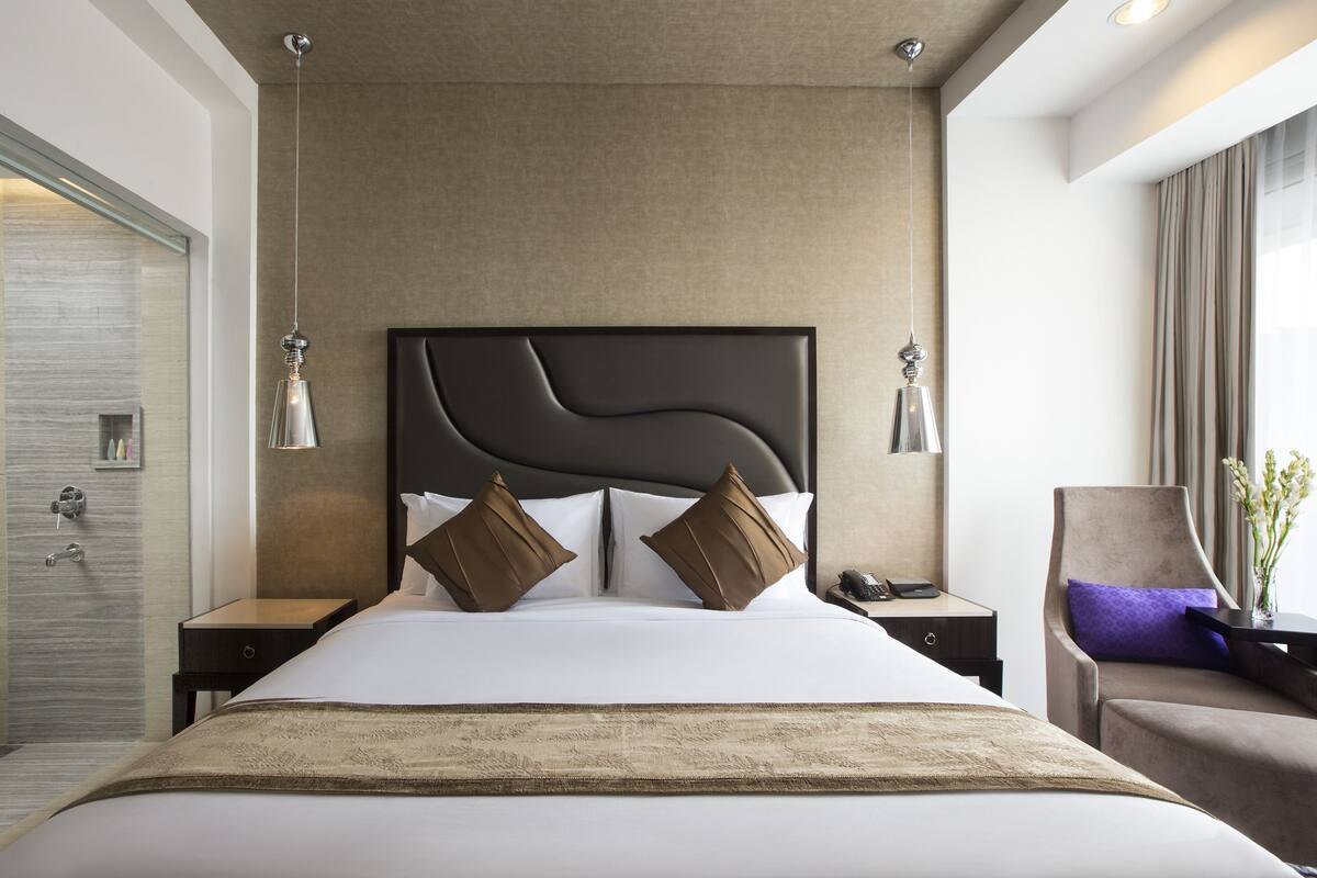 Habitación de hotel moderna con una cama grande, baño independiente, zona de estar y vistas a la ciudad.