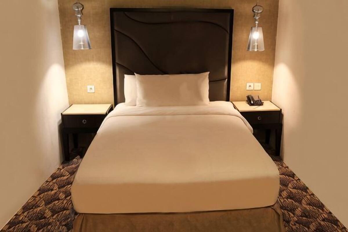 Una habitación de hotel con una cama grande, dos mesitas de noche y lámparas de pared.