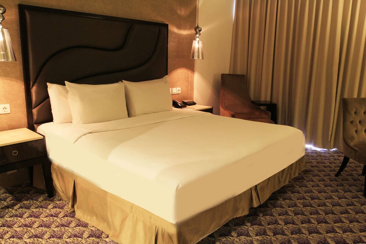 Una habitación de hotel con una cama grande, una mesita de noche, una silla y un escritorio con teléfono.