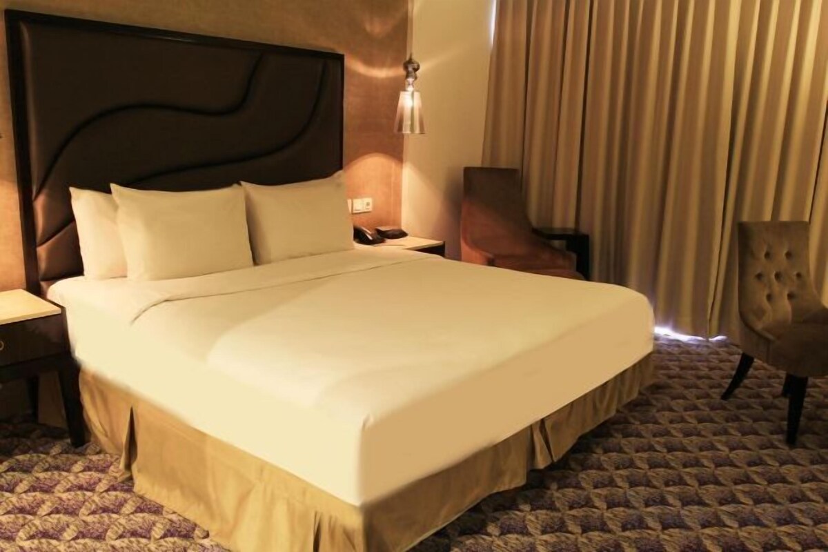 A hotel room with a large bed, a nightstand, a chair, and a lamp.