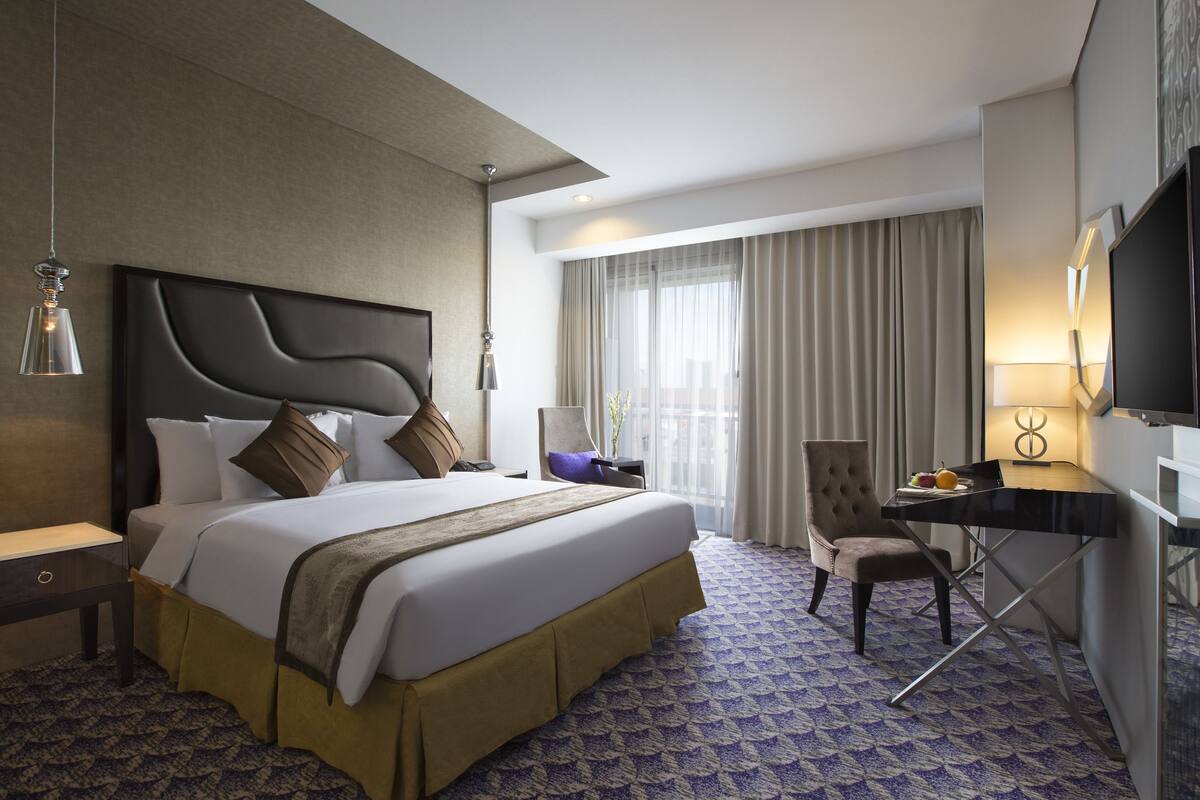 Una habitación de hotel con una cama grande, un escritorio, una silla, un televisor y una ventana con cortinas.