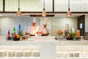 A kitchen area with chefs preparing food, a buffet setup with plates and food items, and a decorative wall with a geometric pattern. - Best Western Chinatown Hotel (Yangon)