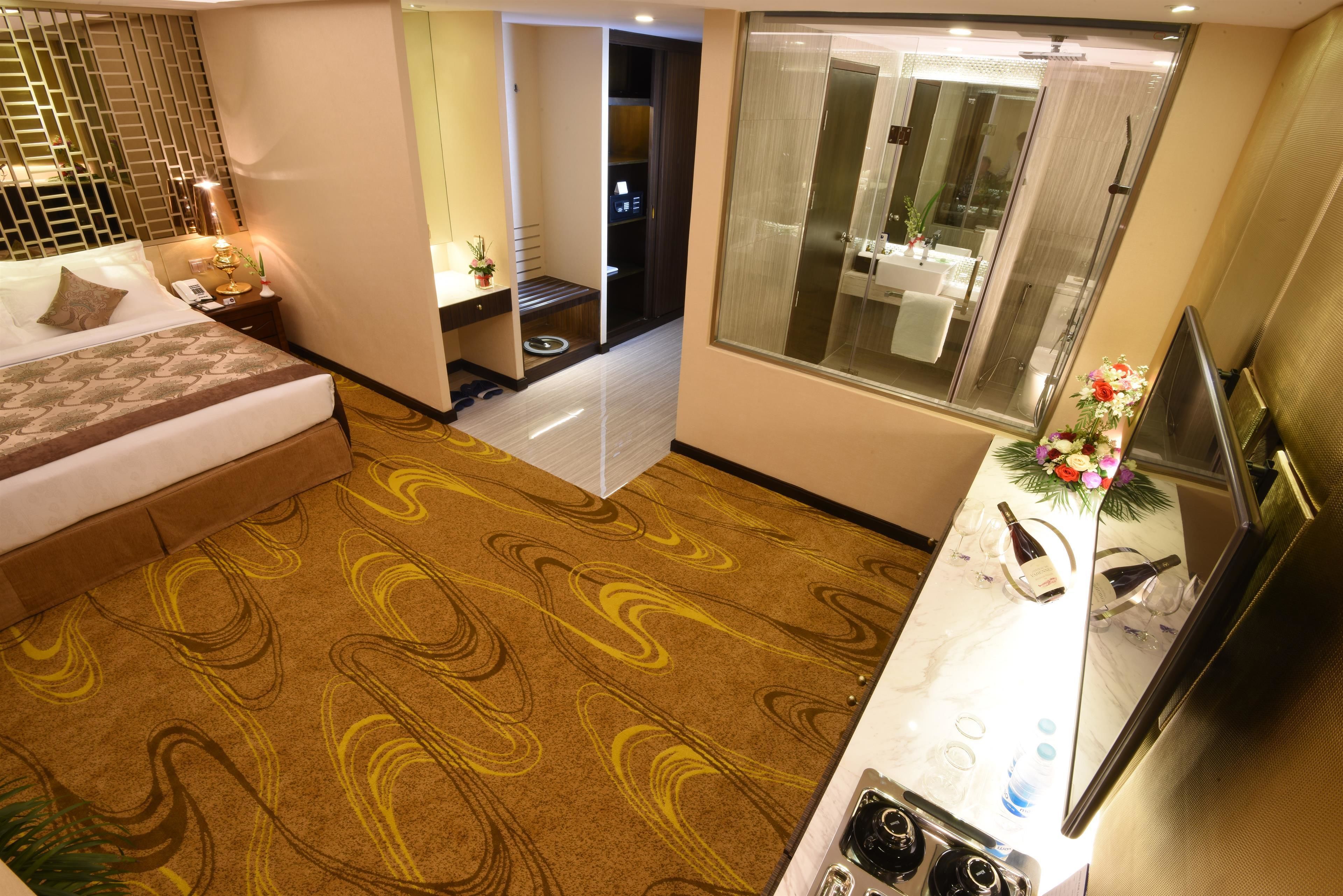 Habitación de hotel con cama, baño con ducha de vidrio, una kitchenette pequeña y televisión.